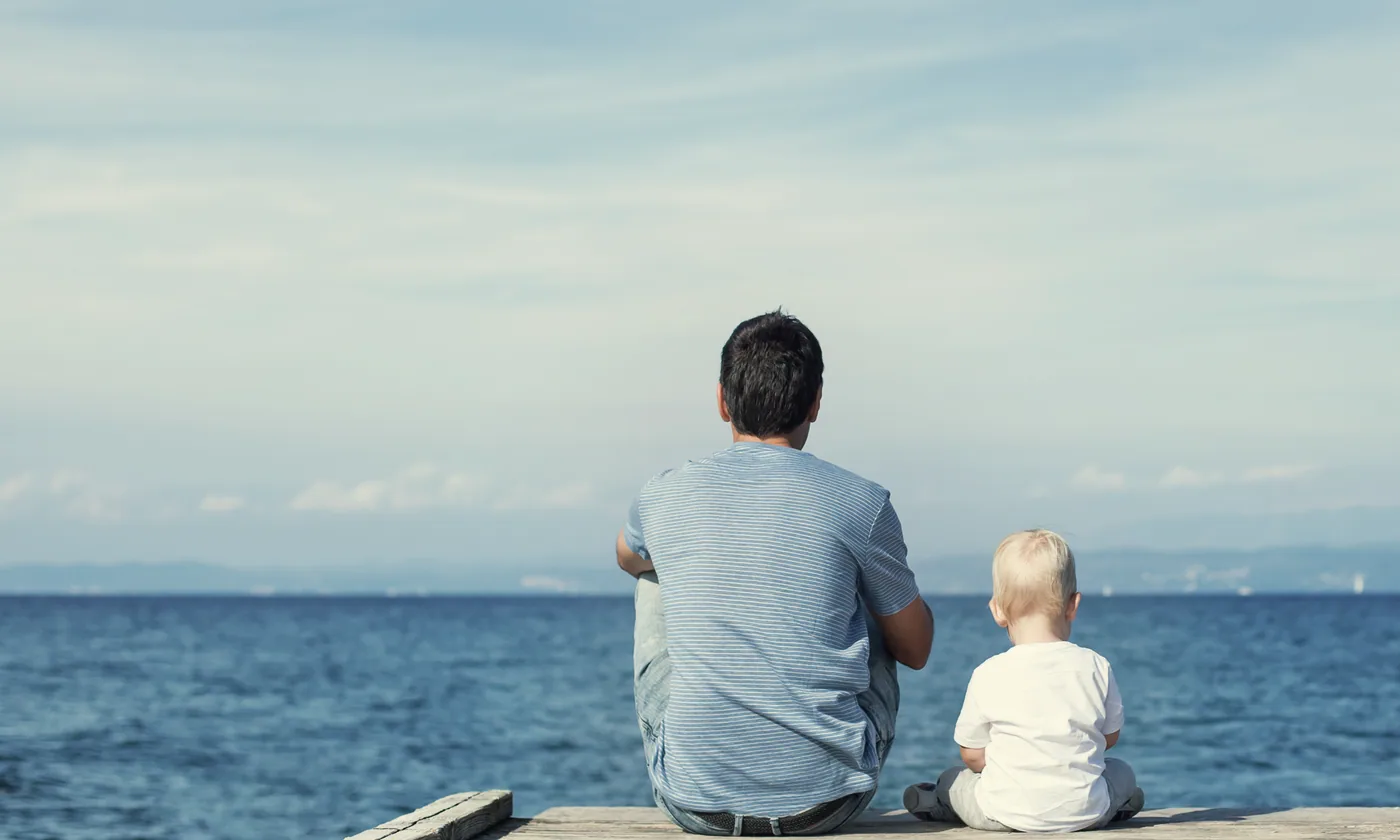 Pai e filho sentados num cais diante do mar