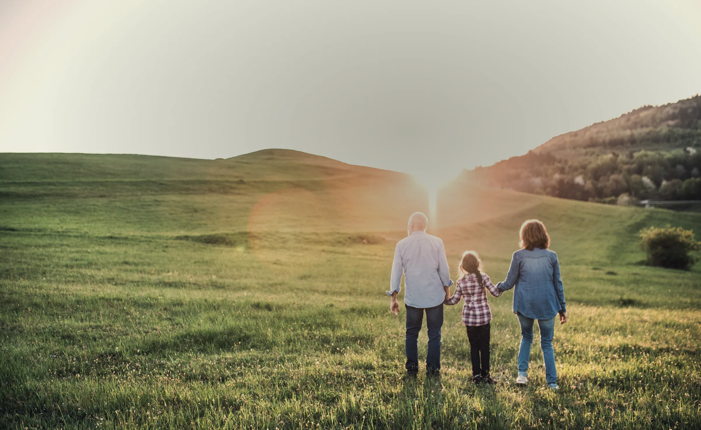 Três gerações de uma família de mãos dadas diante de um campo
