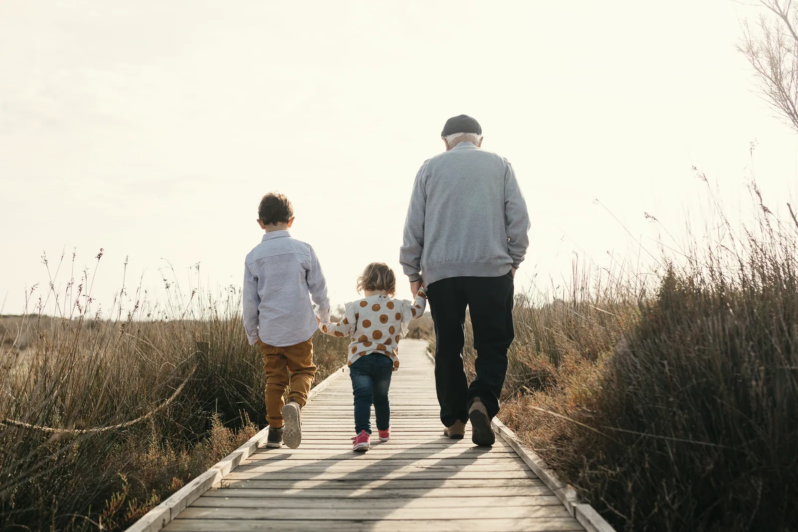 Avô e netos caminhando de mãos dadas por uma passarela de madeira